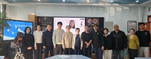 Eleven people standing in a row with one more person on a remote participation window behind.