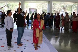 Three people stand on the tarpaulin prepared for the human orrery while roughly 25 people watch