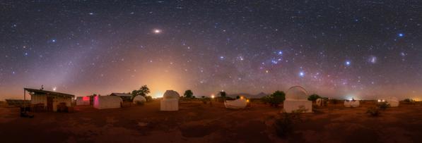 A group of observatories in-front of a dark sky. An arc of light curves from the bottom left. Several stars are visible.
