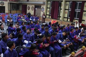 A group of young people in blue robes sit in an assembly hall