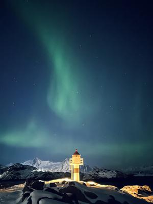 A green wisp of light rises over an illuminated lighthouse