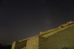 A starry sky, including the diffuse glow of the Milky Way behind a stepped mud brick pyramid.