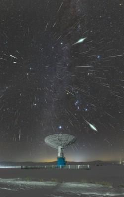 Bright streaks created by meteors radiate from a point in the sky above the dish of a radio telescope.