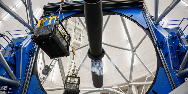 Large curved primary mirror and metal telescope structure at Gemini South. A worker is inspecting the mirror.