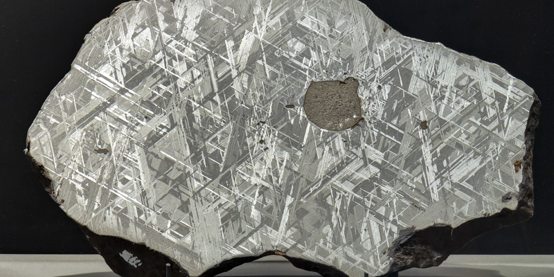A shiny silver cross-section of a meteorite with  two sets of many parallel lines crossing each other