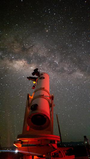 A telescope points to the sky where the Milky Way sits with mottled dark and light patches.