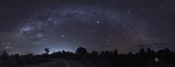The curve of the Milky Way over a road. Bottom left, two bright stars form a line pointing to a kite-shaped stellar assembly