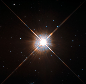 Proxima Centauri appare come un punto luminoso circondato da raggi di diffrazione. Sullo sfondo si vedono diverse stelle più deboli.