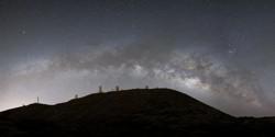Several observatory domes on a mountain top with the arching Milky Way behind.