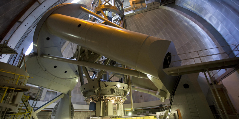 The Hale Telescope mounted inside a large observatory dome, showing its massive optical tube and support structure.