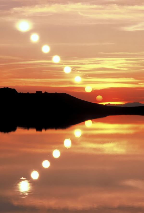 The Sun sinks from the top left of the image towards the middle. This path is reflected in the surface of the lake.