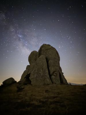 The faint glow of the Milky Way and its mottled dust clouds behind a pillar of rock.